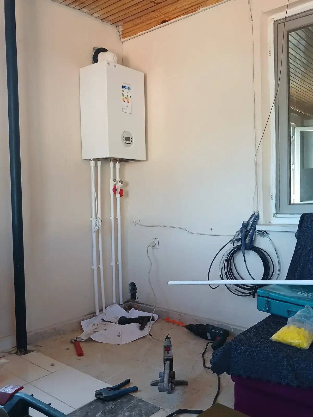 Yeni takılmış beyaz kombi, tesisat boruları ve yerdeki montaj aletleri