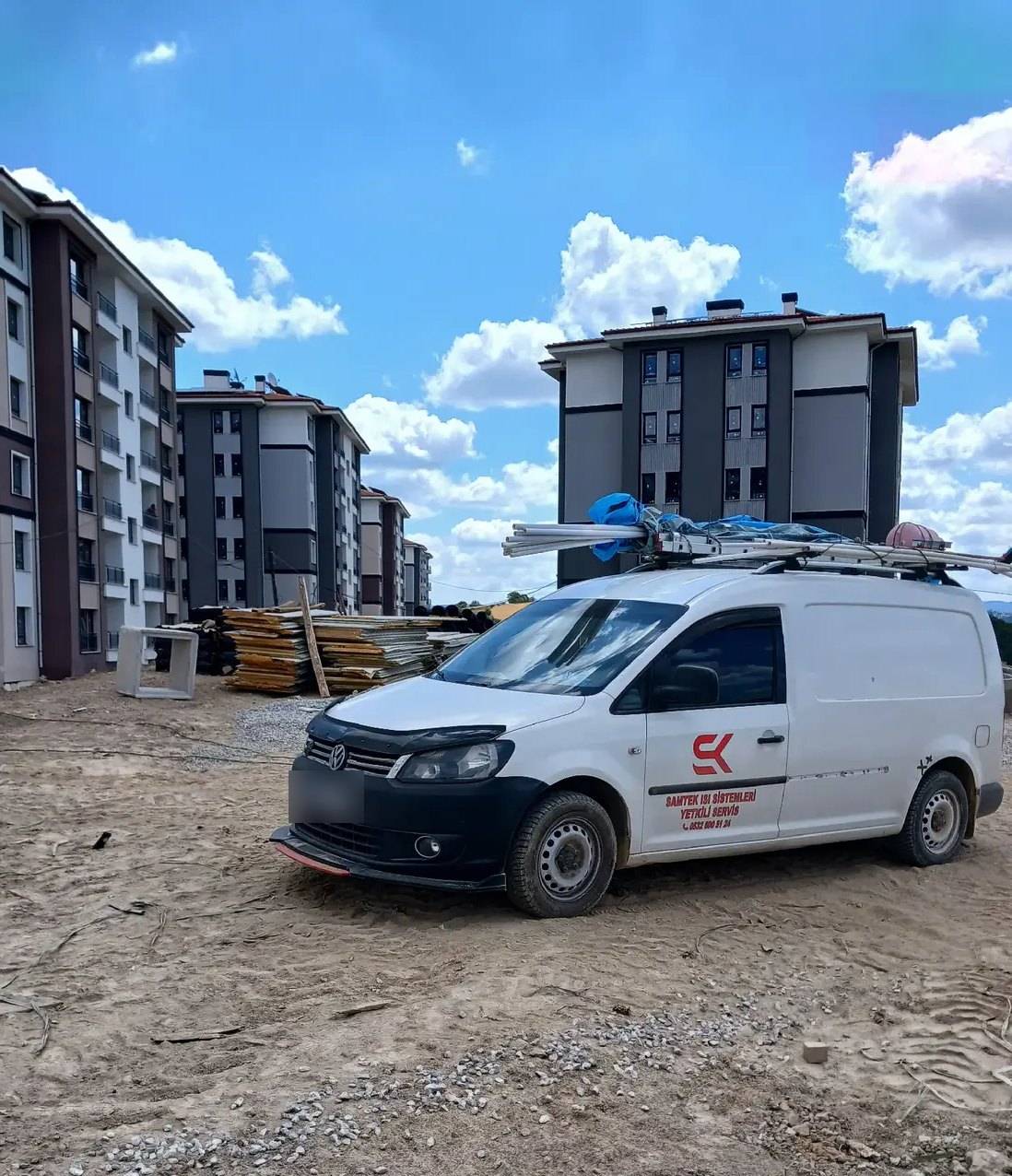 Yeni yapılan apartmanların önündeki toprak alanda, üzerinde borular taşıyan SAMTEK servis aracı